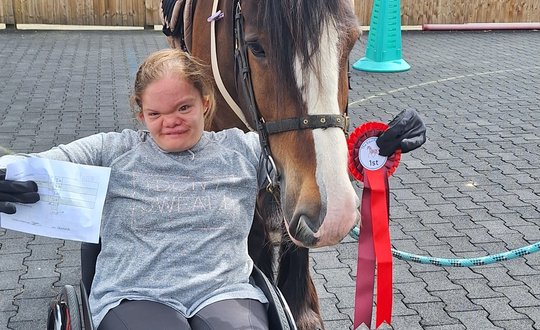 Young person in a wheelchair with horse and rosette