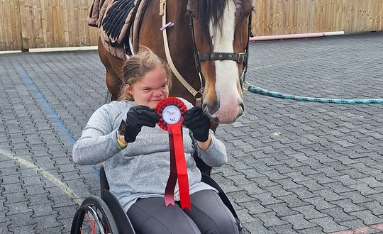 Young person in a wheelchair with horse and rosette
