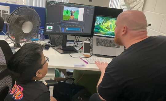 two people editing a video on a big computer screen