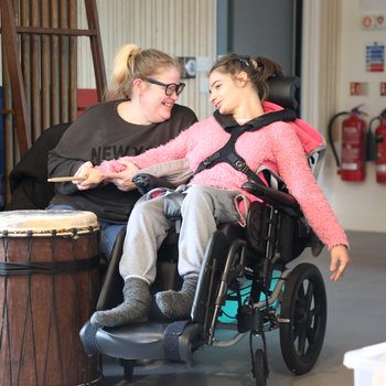 Young girl wearing a pink jumper and in a wheelchair in drumming class