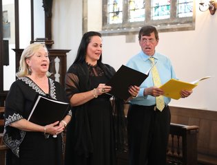 Two women and a man are singing in a church